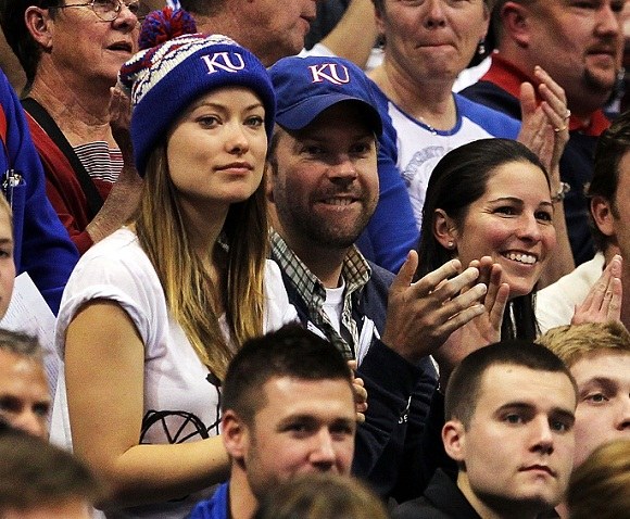 Mėlynomis kepuraitėmis pasipuošę Jasonas Sudeikis ir Olivia Wild stebi krepšinio rungtynes. / AFP/„Scanpix“ nuotr.