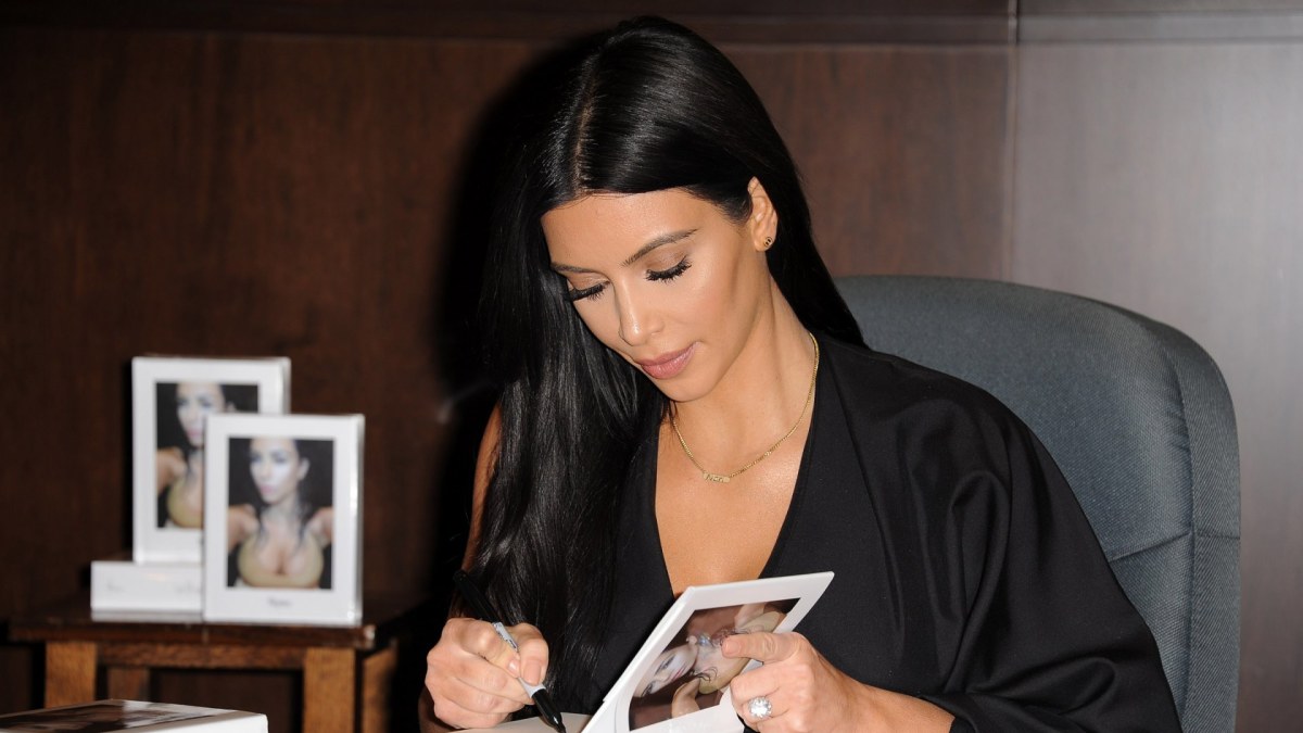Kim Kardashian pasirašo ant savo knygos „Selfish“ / „Scanpix“ nuotr.