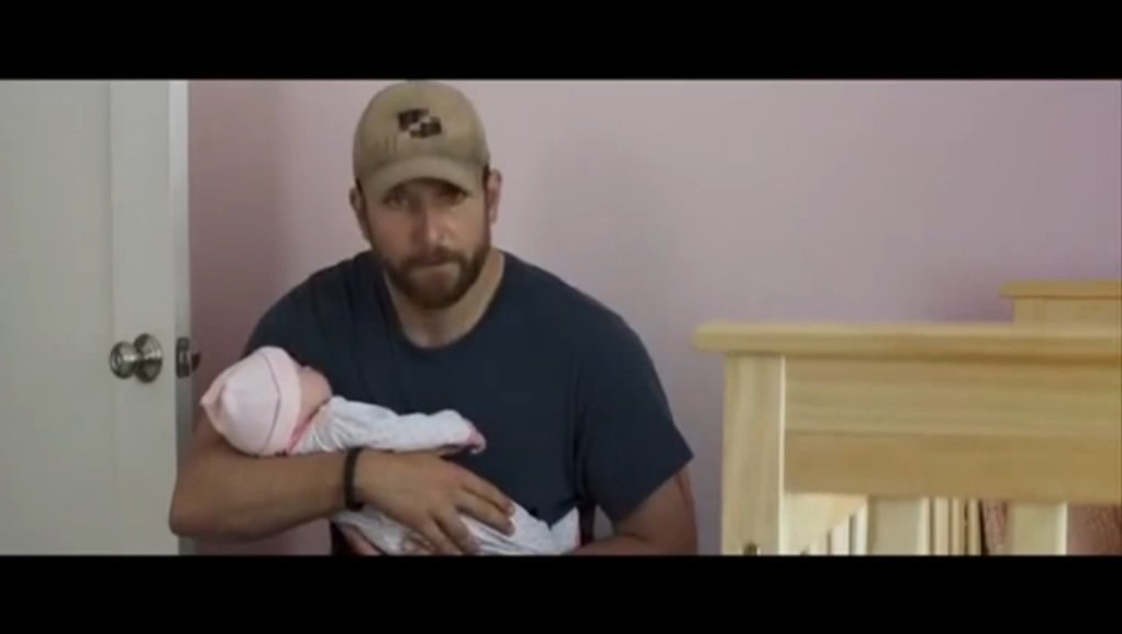 Bradley Cooperis su netikru kūdikiu ant rankų filme „Amerikiečių snaiperis“ / Kadras iš filmo